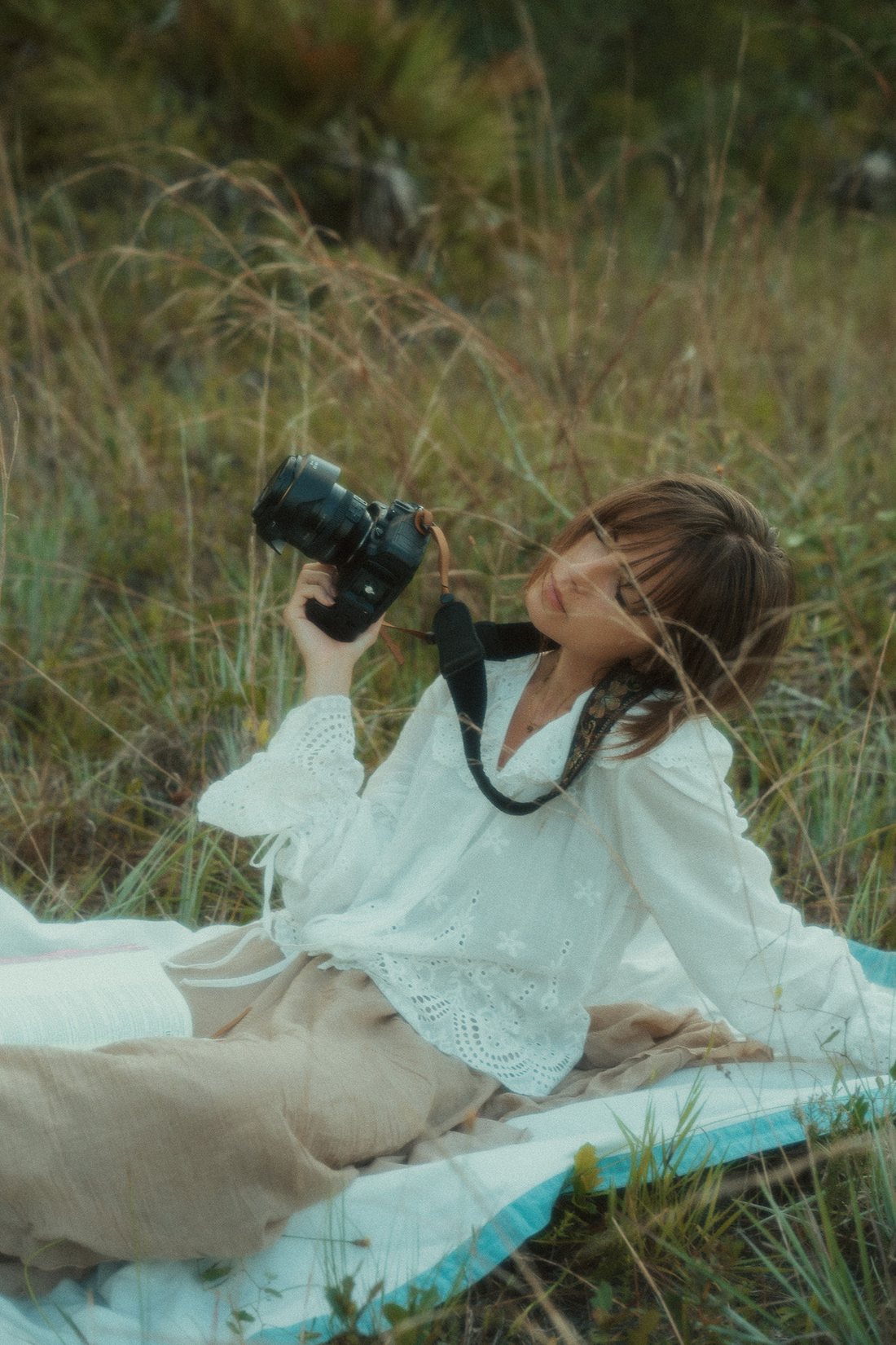 Marija, photographer at MZO Photos, lying in tall grass holding her camera